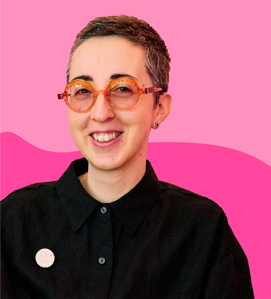 Hannah smiling, wearing orange glasses, with short brown hair, and colourful pink shapes background.