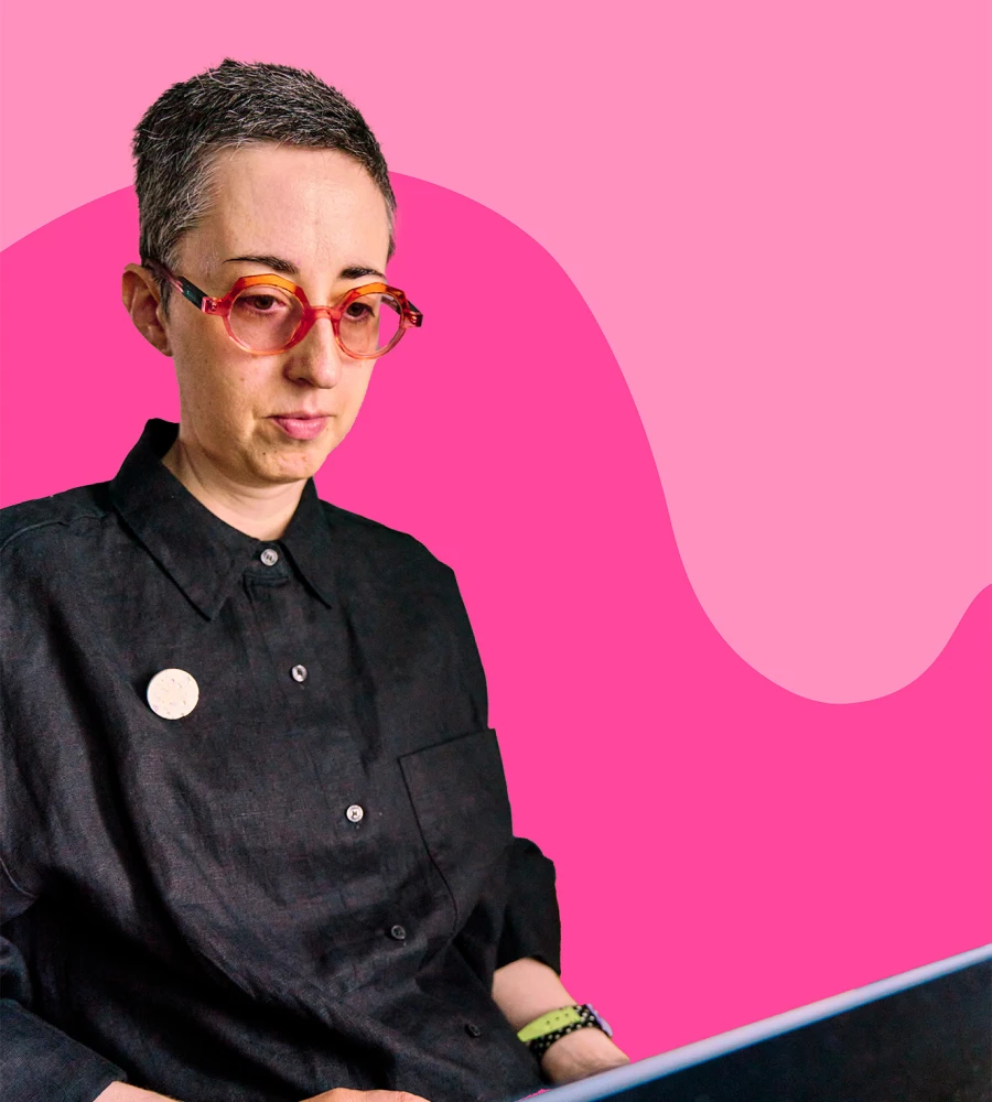 Hannah working on her laptop in her office, concentrating, with pink shapes in background.