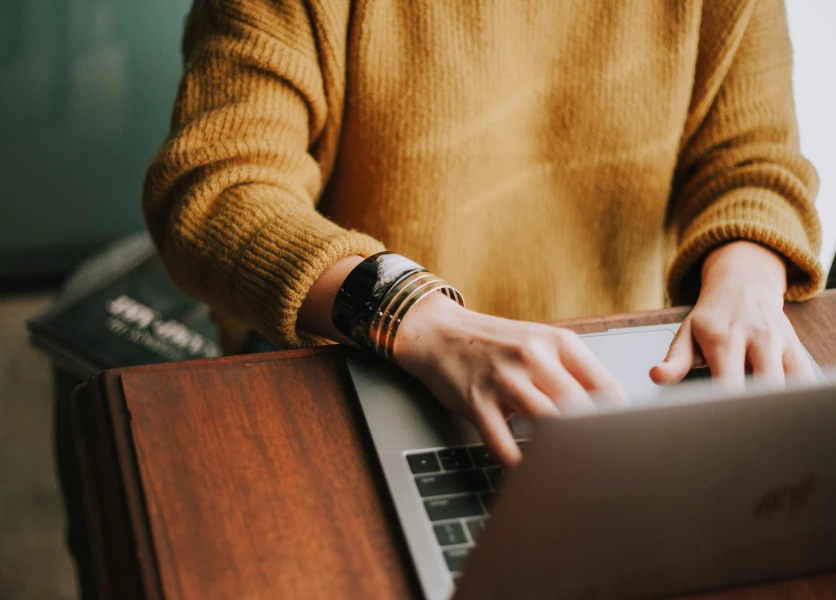 A person wearing a warm yellow jumper typing on a laptop.
